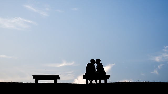 Two people kissing on a bench with a blue sky in the background