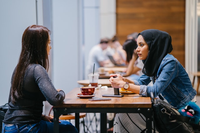 Twee meisjes aan een tafel, waarvan eentje met hoofddoek en een ander zonder. Gebruikt voor het verhaal Flora en Nawar.